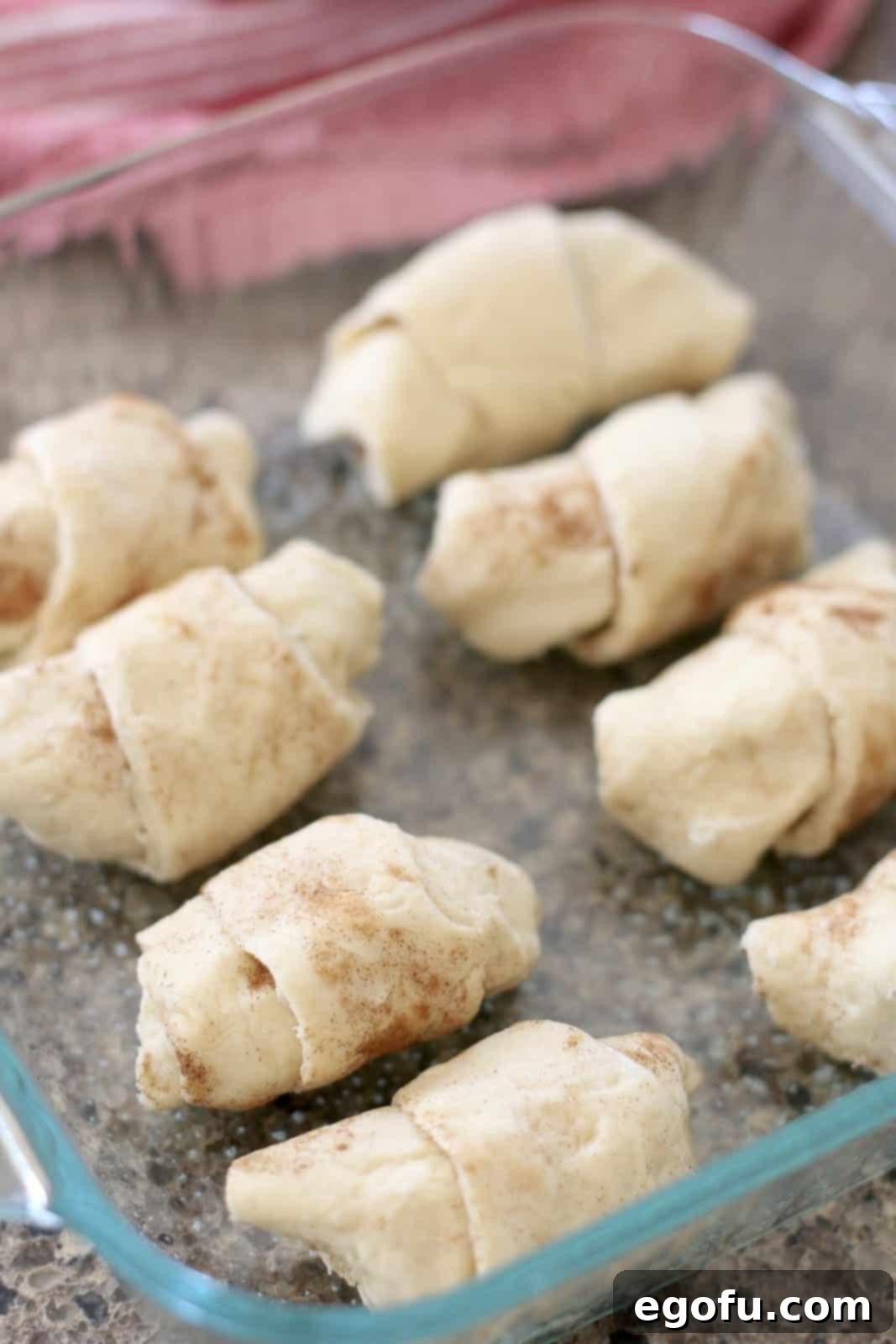 Sweet Apple Pockets 9 Eight neatly rolled crescent roll apple dumplings arranged in two rows within a clear glass baking dish, ready for the next steps in the recipe.