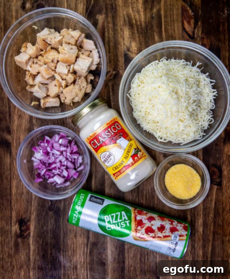 Layout of ingredients: refrigerated pizza dough, garlic alfredo sauce, shredded mozzarella cheese, grilled chicken, red onion, corn meal.