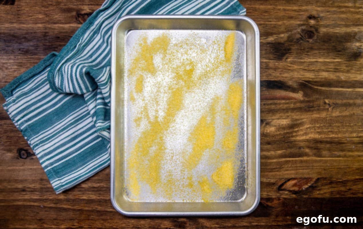 Yellow corn meal sprinkled on top of stainless steel baking sheet.
