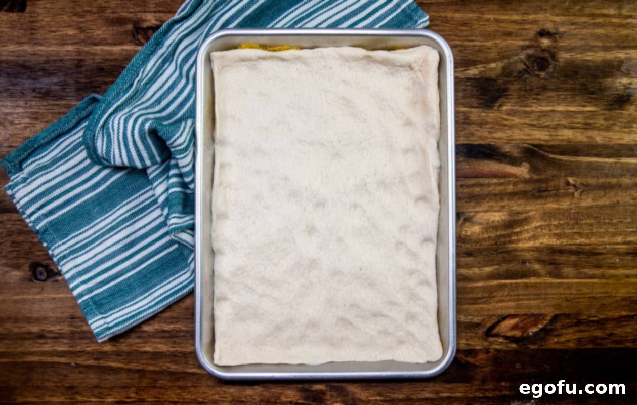 Pizza dough spread out evenly onto baking sheet.
