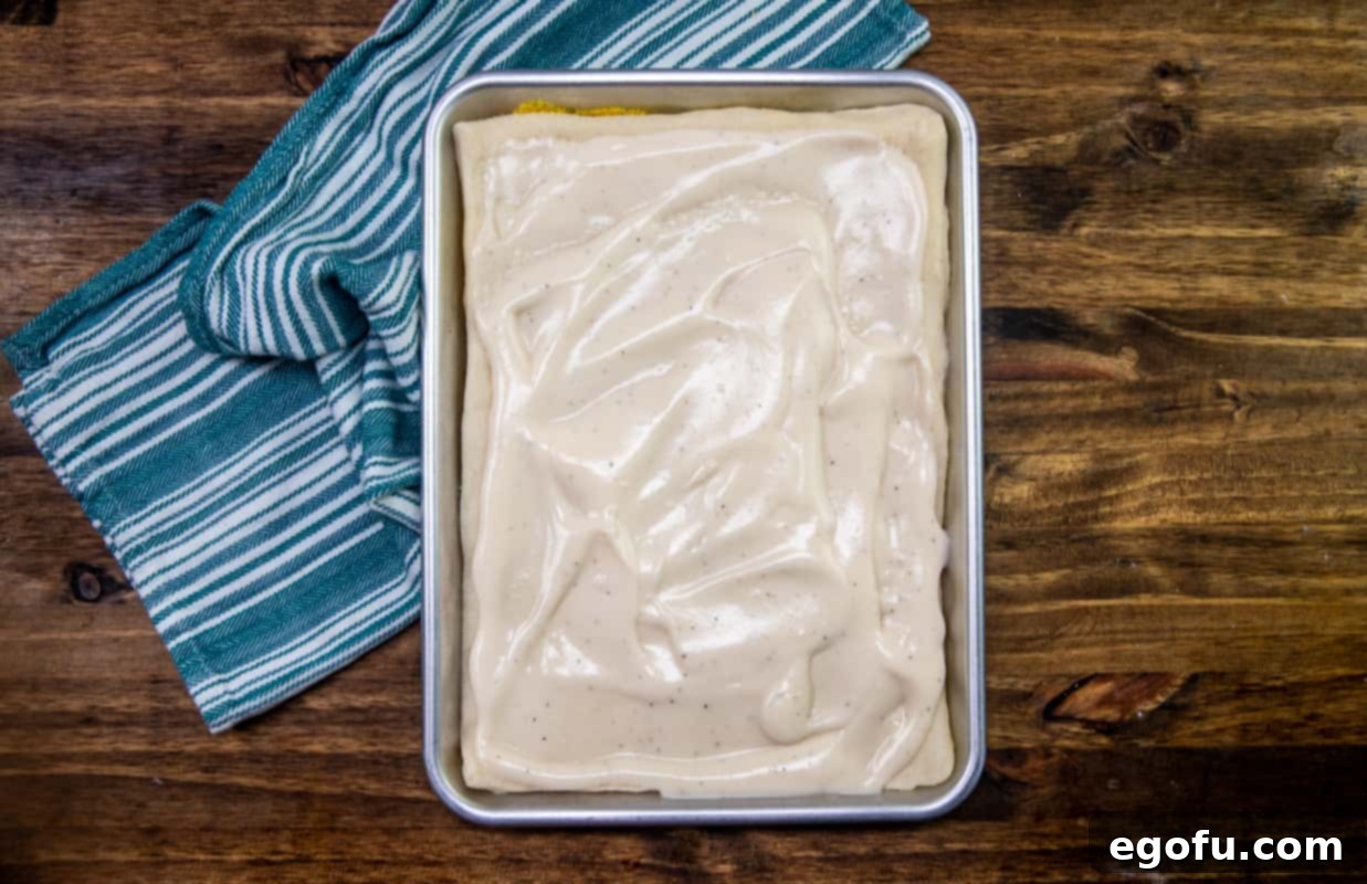 Alfredo sauce evenly spread on top of pizza dough on a baking sheet.