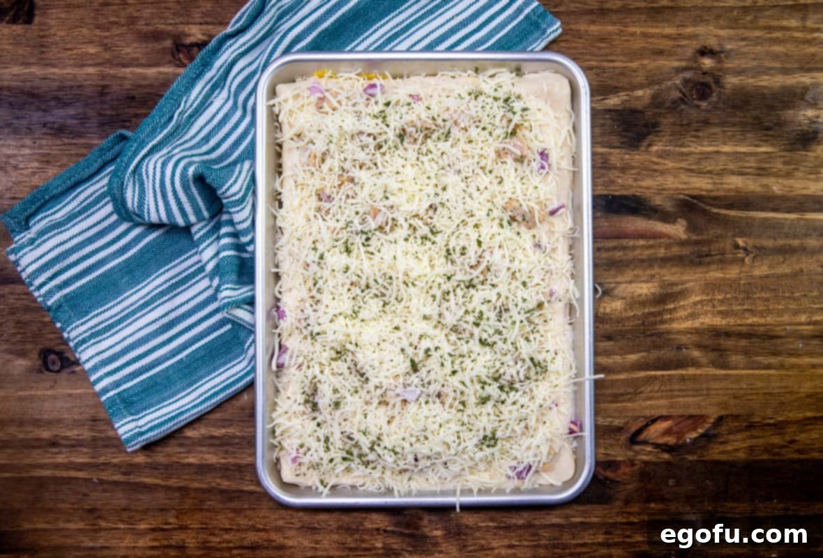 Shredded mozzarella cheese and dried parsley sprinkled evenly on top of pizza before baking. 