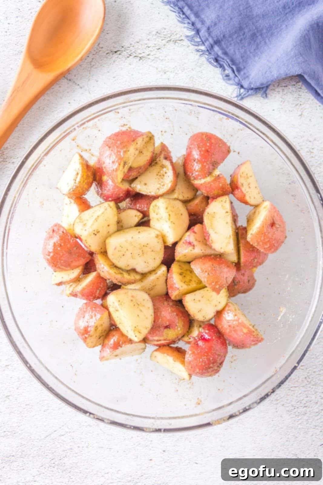 Potatoes in a bowl, now seasoned with salt, pepper, celery seeds, and ground thyme, all mixed together evenly.