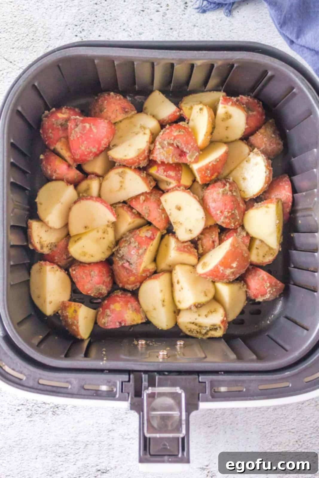 Heavily coated red potatoes carefully placed in a single layer within the air fryer basket, ready for cooking.