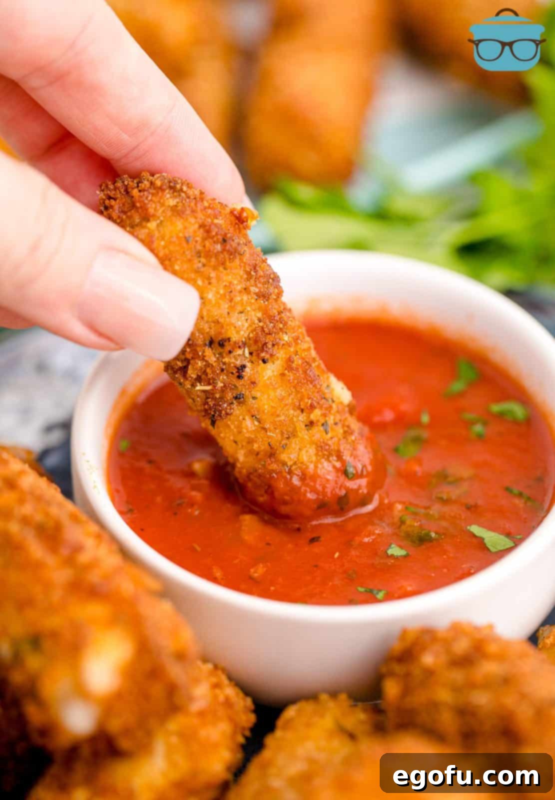Hand dipping one Homemade Mozzarella Stick in sauce.