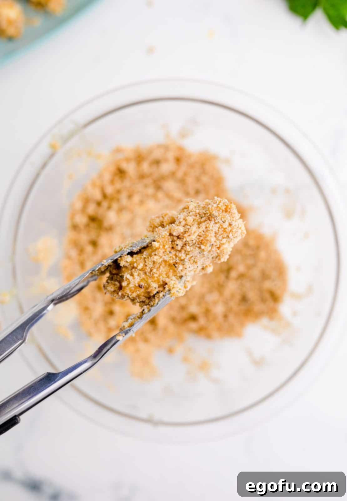 Tongs holding up coated cheese stick.