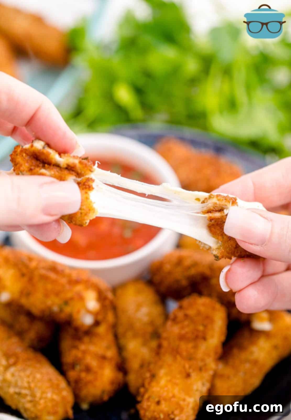 Hand pulling one Homemade Mozzarella Stick apart showing cheese pull.
