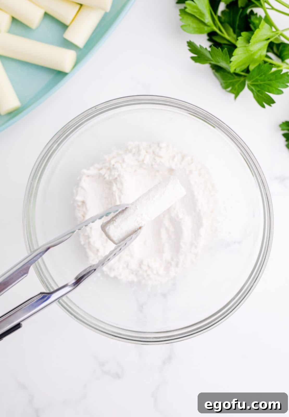 Tongs dipping cheese in flour.