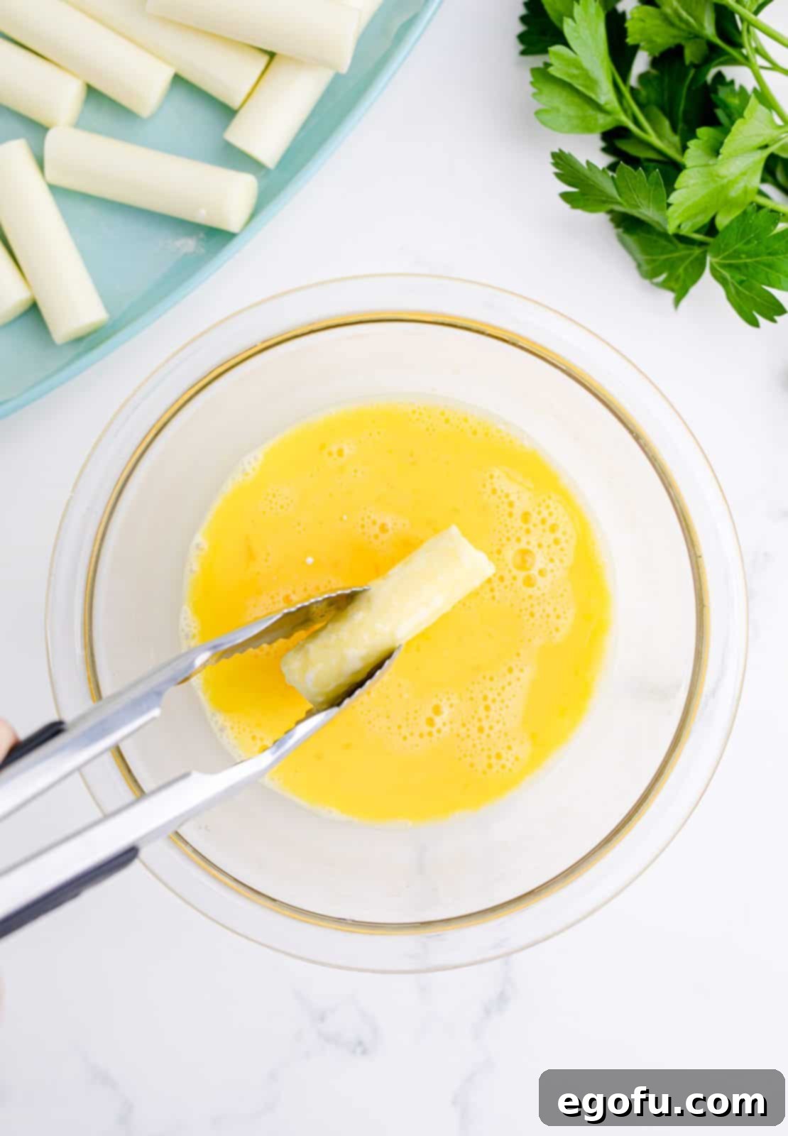 Tongs dipping cheese in egg mixture.