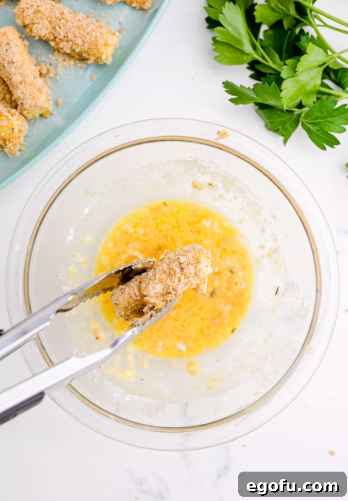 Tongs dipping cheese back into breadcrumb mixture.