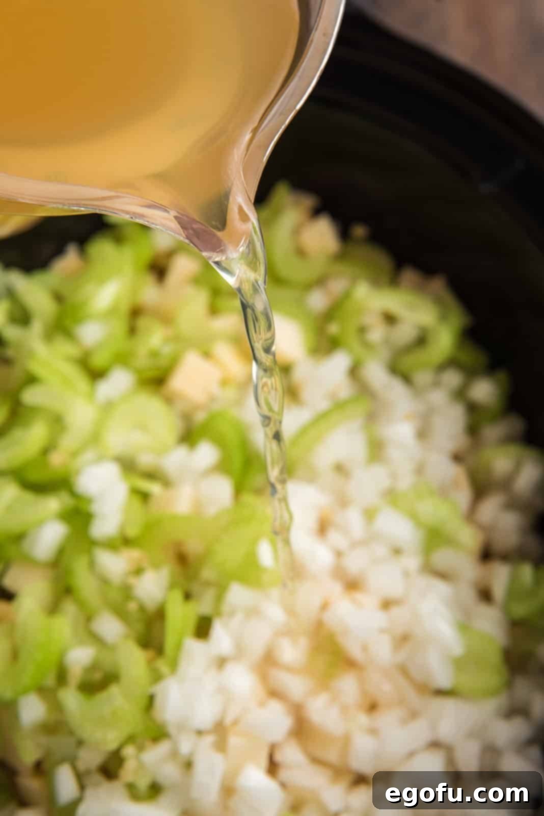Slow Cooker Creamy Potato Bliss 5 The cooking process begins as chicken broth is poured over a mixture of diced potatoes, onions, celery, and garlic in a slow cooker.