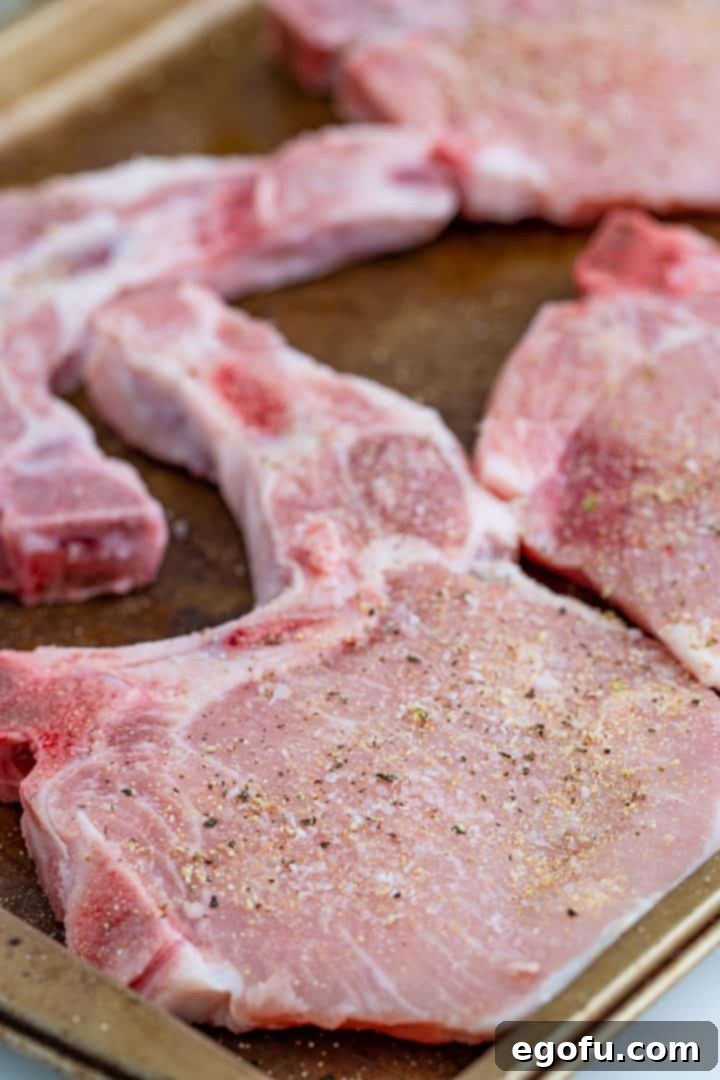 Thick-cut pork chops, generously seasoned with salt, pepper, and garlic powder, laid out on a cookie sheet, ready for searing.