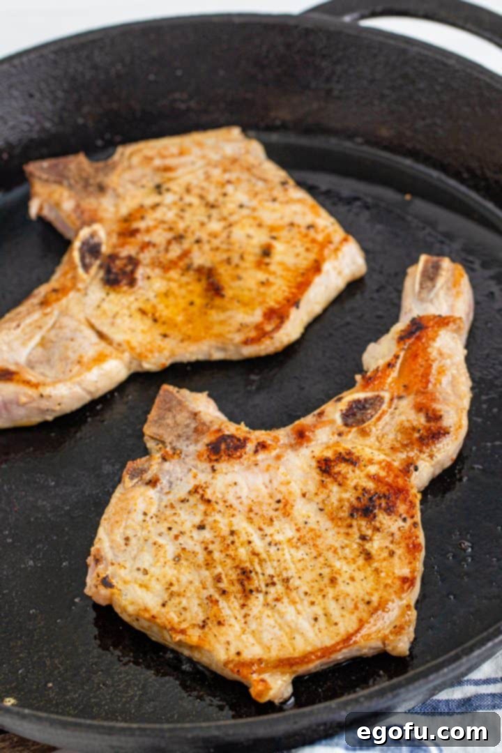 Two thick-cut pork chops browning perfectly in a hot cast iron skillet, developing a savory crust.
