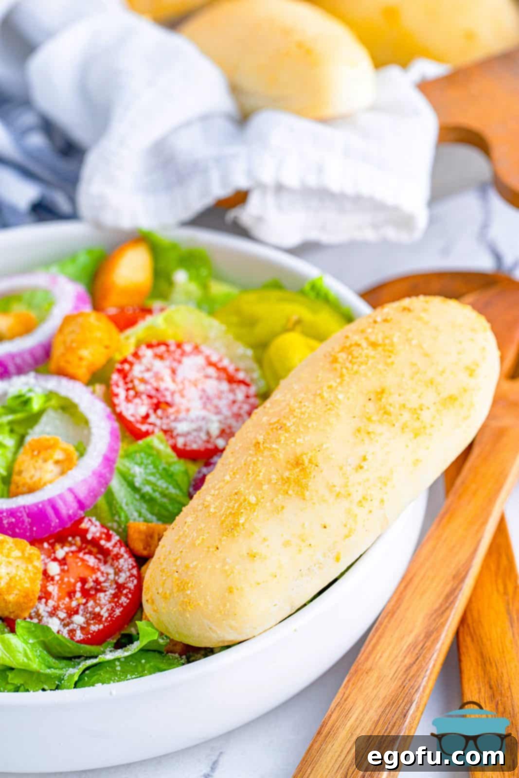 a breadstick on the side of a white bowl holding a salad. 