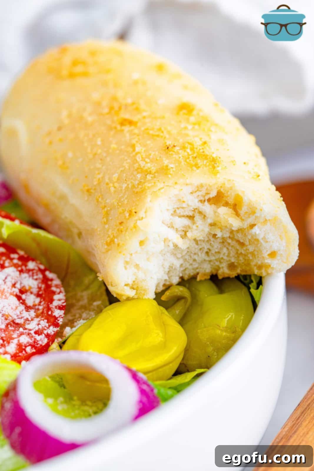 closeup photo of a breadstick that has had a bite removed and sitting on the side of a bowl of salad. 