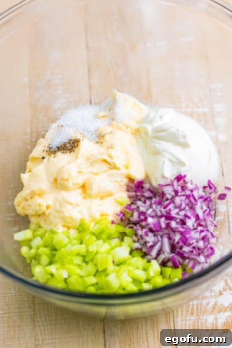 Glass bowl with celery, red onion, sour cream, salt, pepper, and mayo.