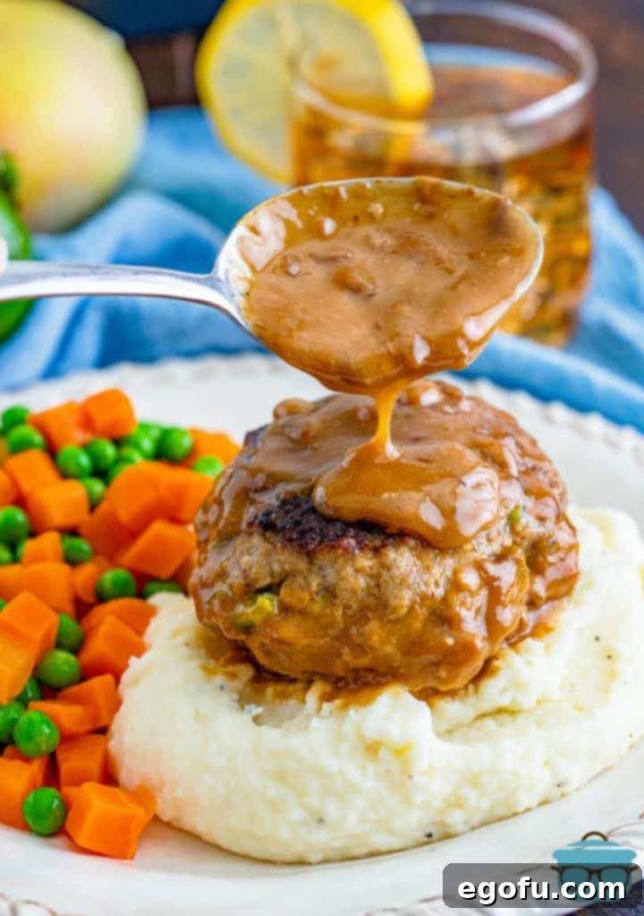 a spoon pouring gravy over a cooked hamburger on mashed potatoes. 