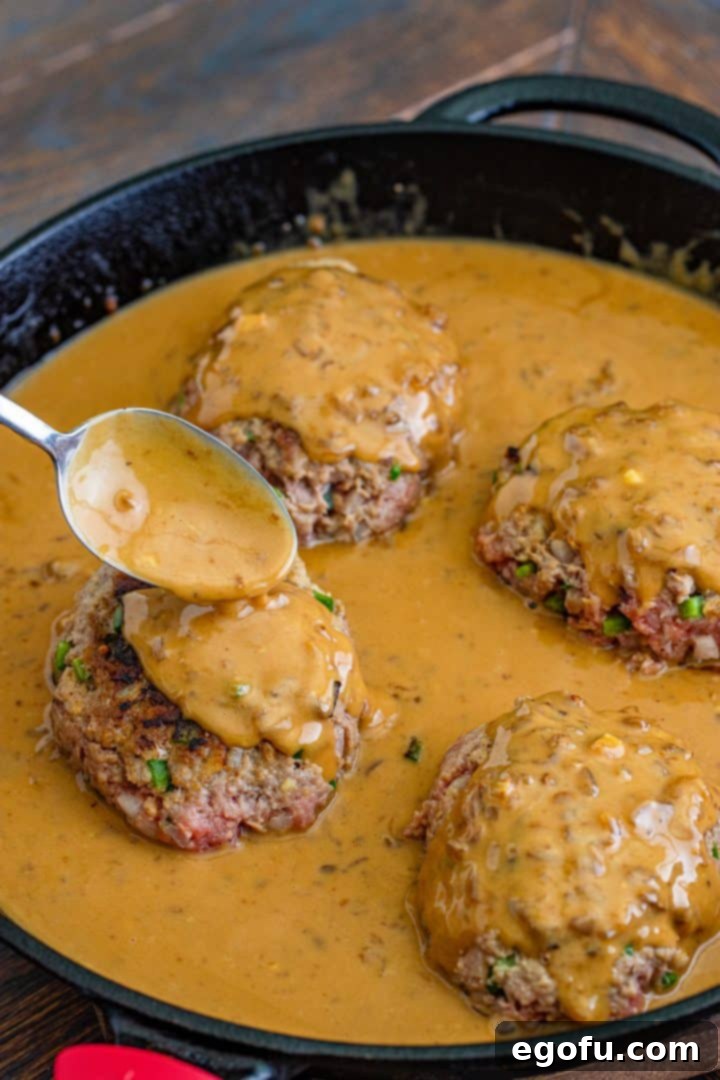 spooning gravy over hamburger steaks in black cast iron skillet. 