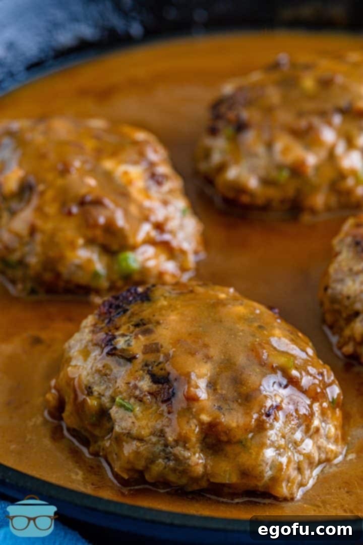 four hamburger patties in a cast iron pan and covered in gravy.