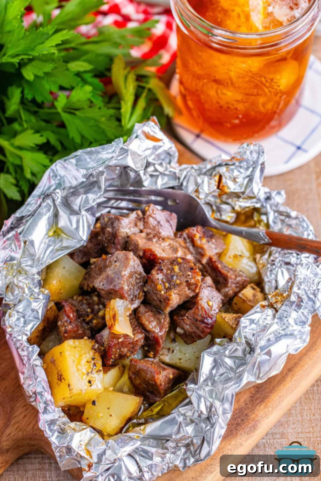 an overhead view of cooked steak and potato bites in aluminum foil packet with fresh parsley in the background.