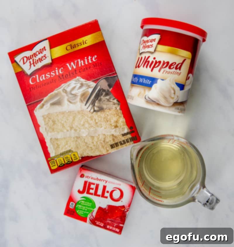 Strawberry Burst Poke Cupcakes 4 Key ingredients for Strawberry Jell-O Poke Cupcakes laid out: a box of white cake mix, a container of whipped white frosting, a box of strawberry Jell-O, and egg whites in a bowl.