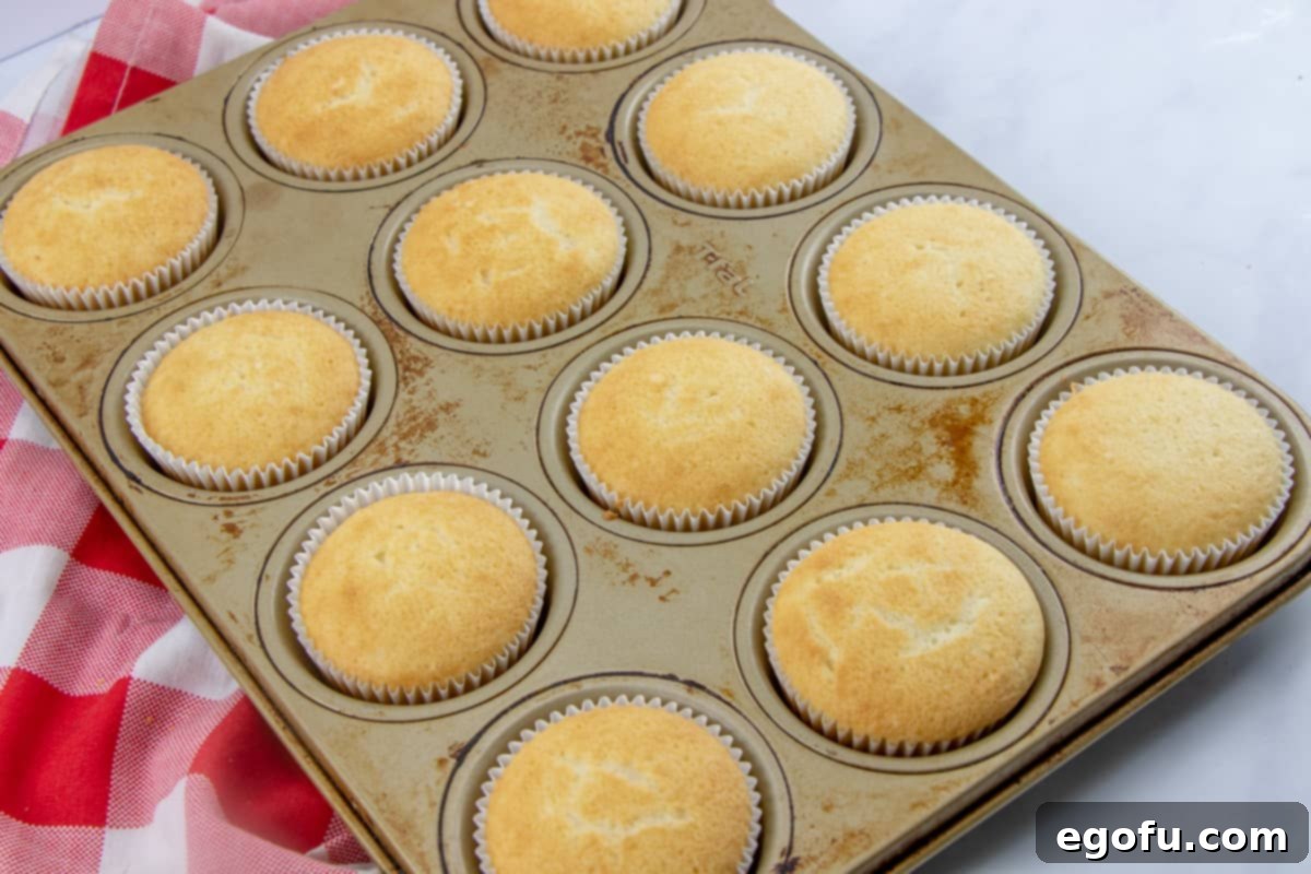 Strawberry Burst Poke Cupcakes 5 A dozen freshly baked golden-brown cupcakes sitting in a muffin pan, cooling down.