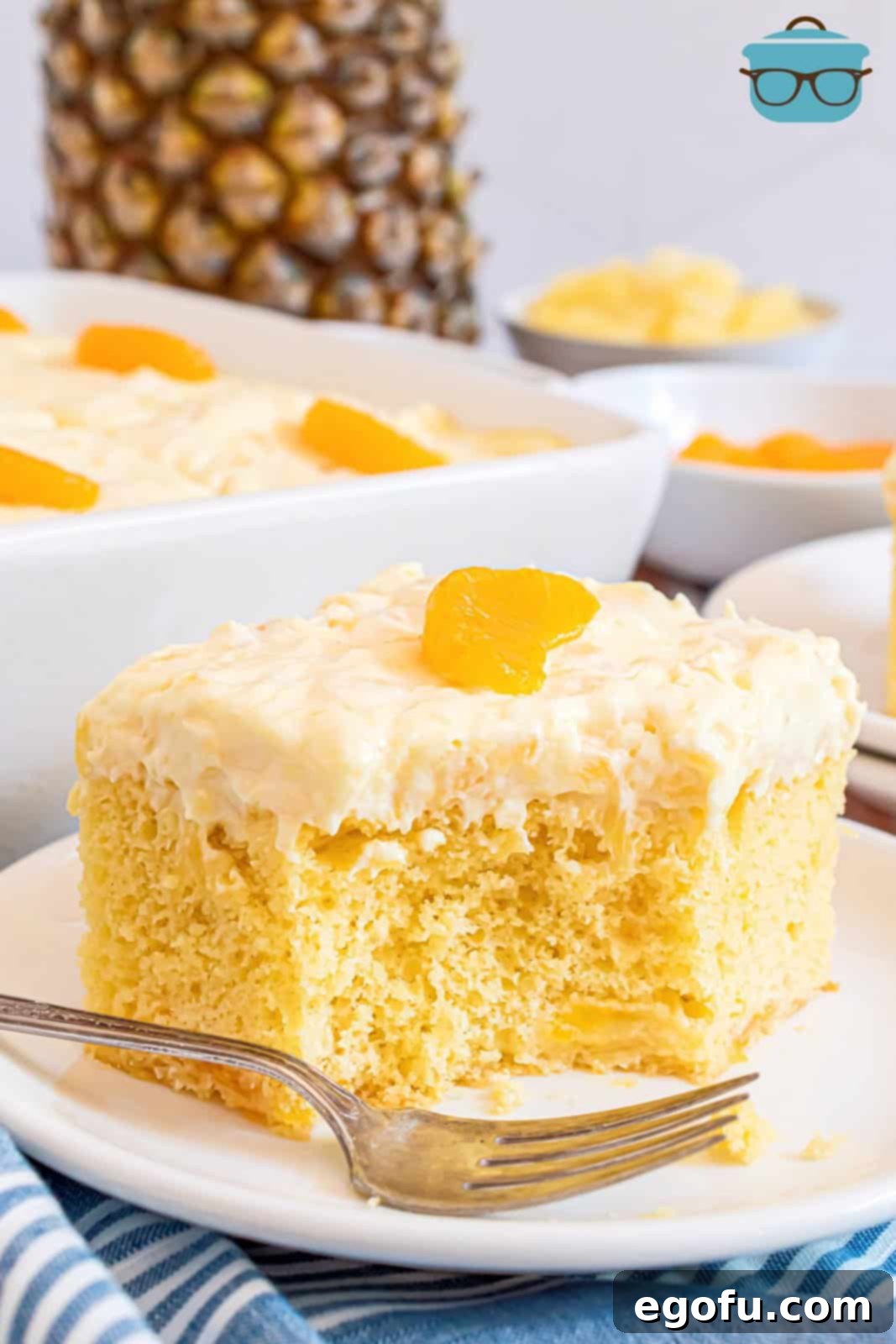 Pineapple Mandarin Ambrosia Cake 2 A perfectly portioned slice of Pig Picking Cake (also known as Mandarin Orange Cake) presented on a crisp white plate, with a small bite removed, showcasing its moist texture and vibrant fruit.