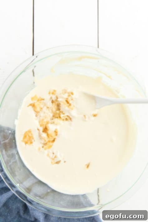 Pineapple Mandarin Ambrosia Cake 16 Drained crushed pineapple being stirred into the prepared frosting mix in a bowl.