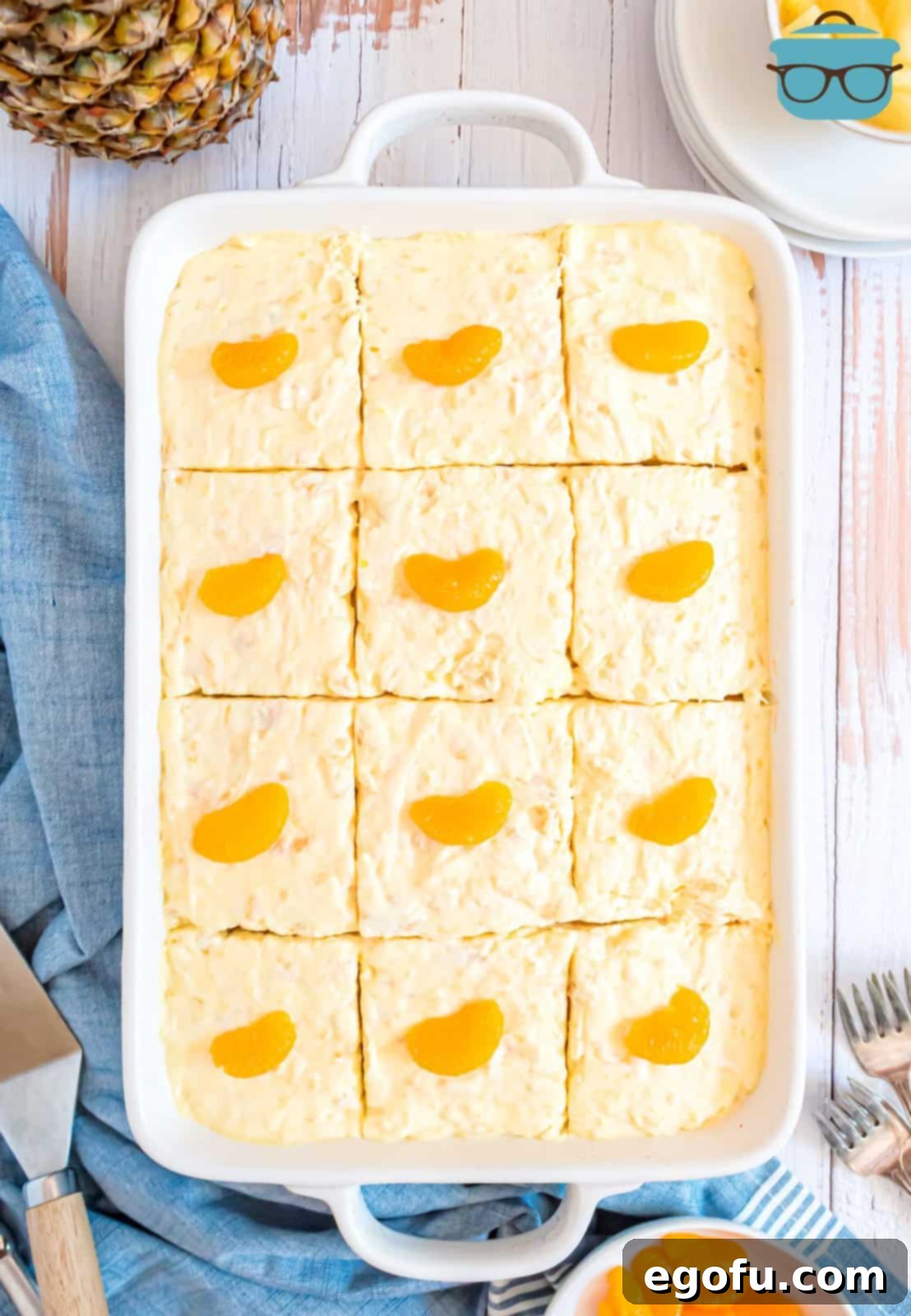 Pineapple Mandarin Ambrosia Cake 8 A close-up shot of a beautifully frosted and sliced Pig Pickin' Cake, with each individual slice topped with a vibrant mandarin orange segment, ready to be served.