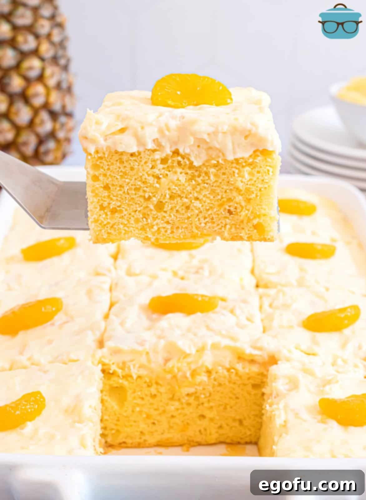 Pineapple Mandarin Ambrosia Cake 9 A metal spatula gracefully lifts a single slice of the delectable mandarin orange cake from the baking dish, highlighting its moist layers and creamy topping.
