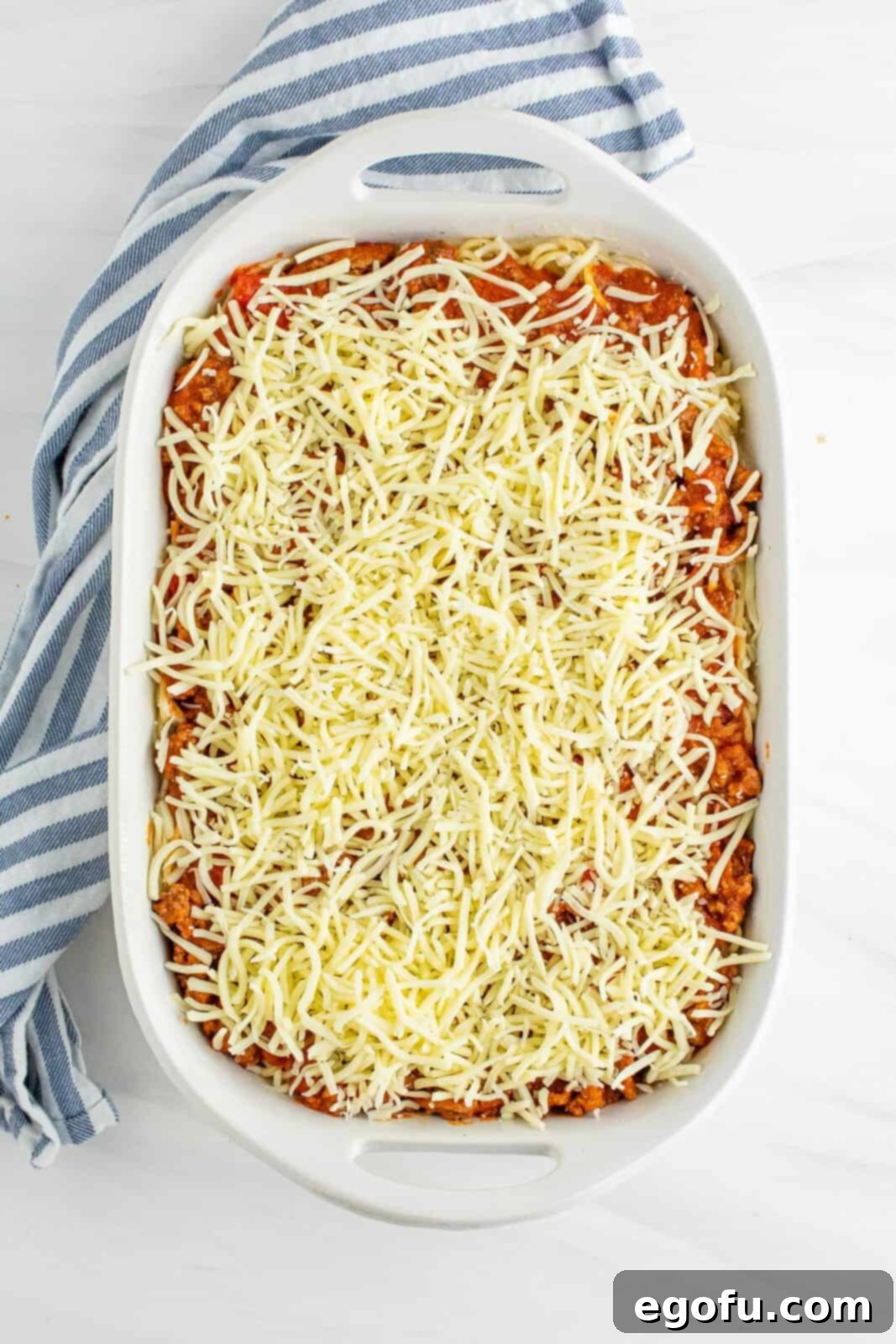 Shredded mozzarella cheese generously distributed on top of the layers of spaghetti sauce and Alfredo noodles.