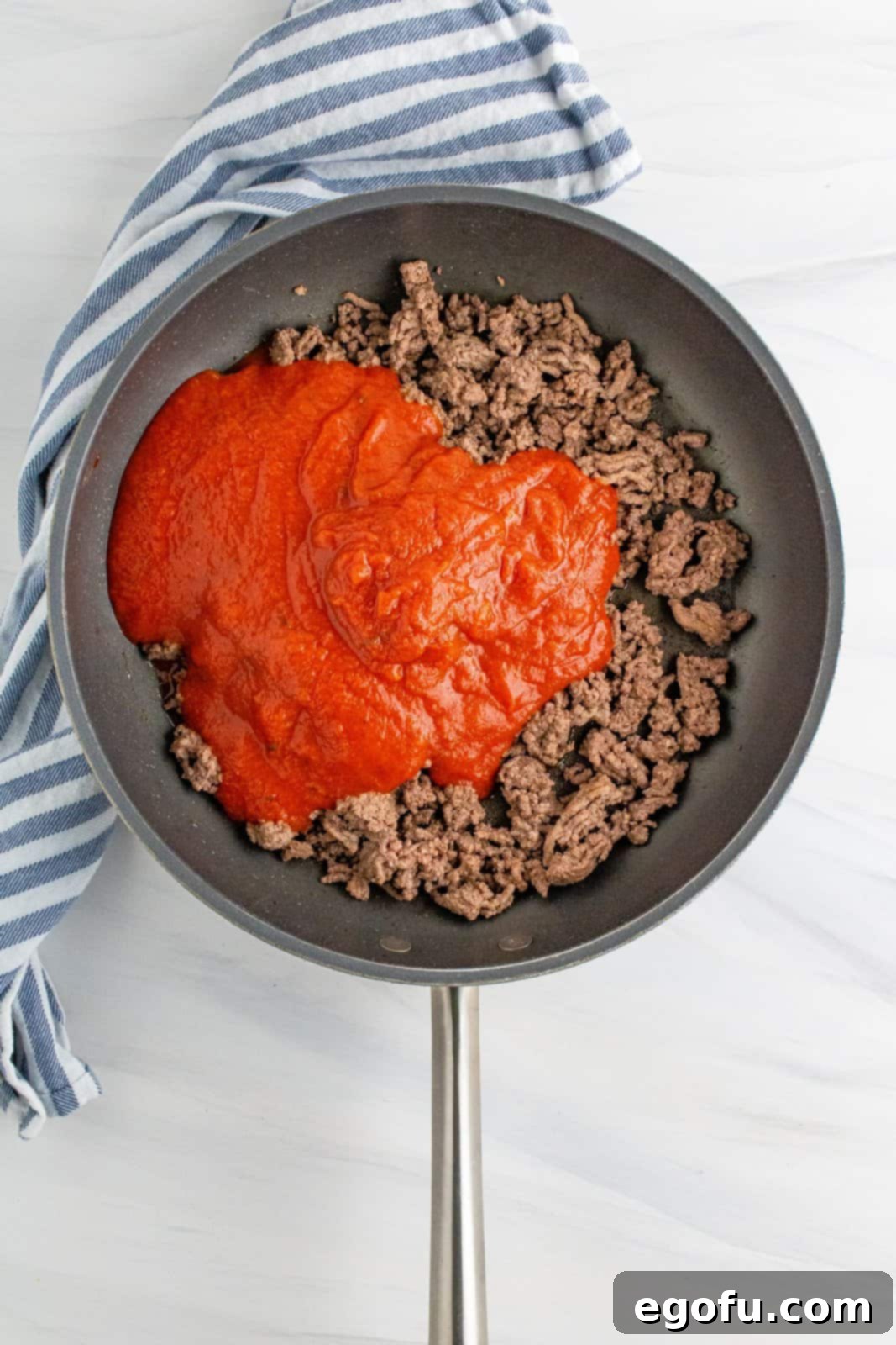 Spaghetti sauce added to the ground beef in the large skillet, being stirred to combine.