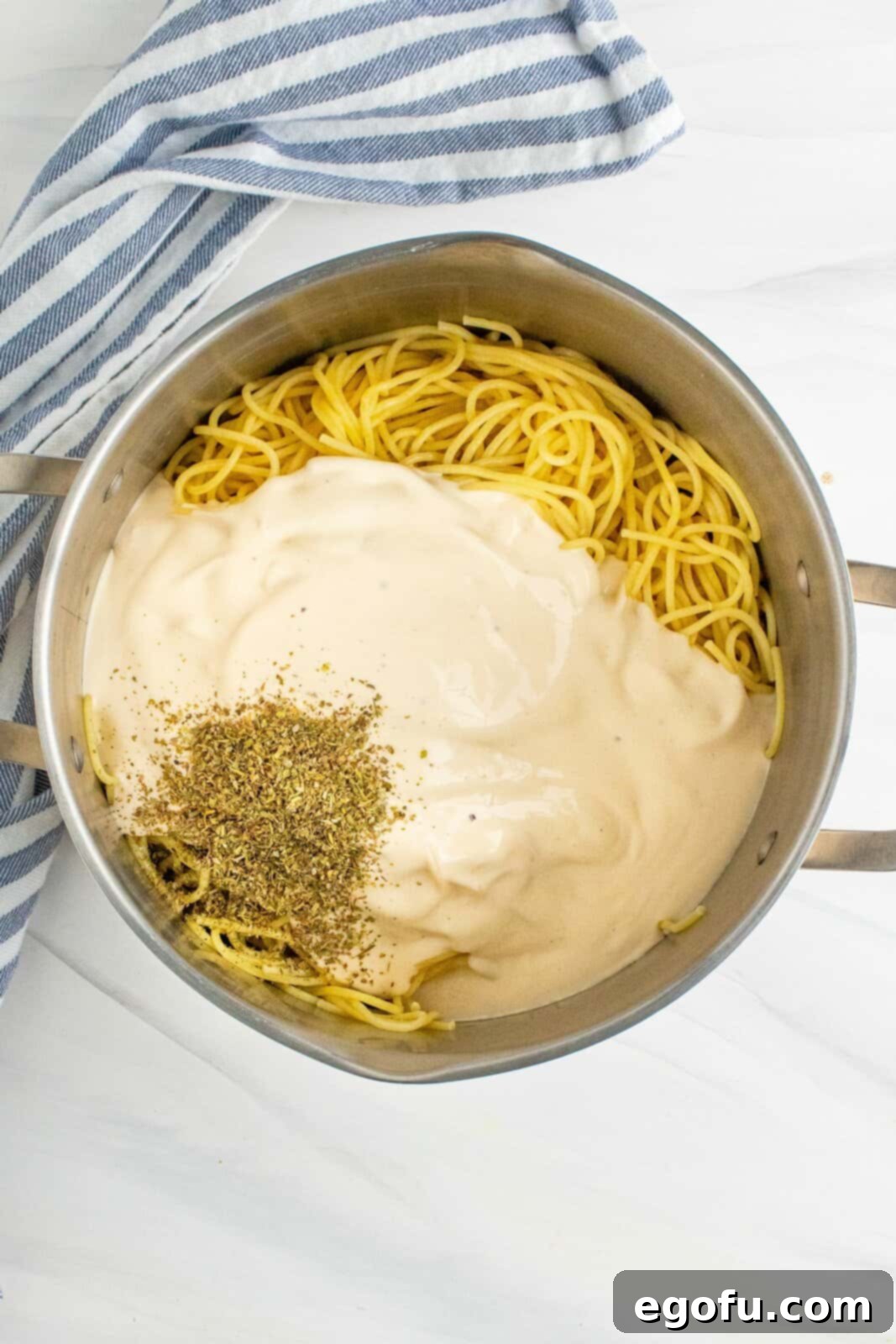 Alfredo sauce and Italian seasoning stirred together with cooked spaghetti noodles in a large stock pot, creating a creamy coating.