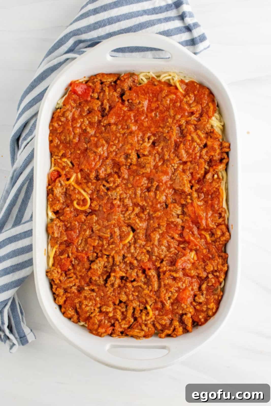 Meat sauce spread on top of Alfredo noodles in the baking dish, creating the second layer.