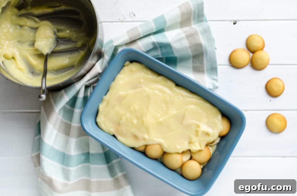 Velvet Banana Pudding Perfection 7 spreading homemade custard layer over sliced bananas and Nilla wafers in a 2-quaer casserole dish
