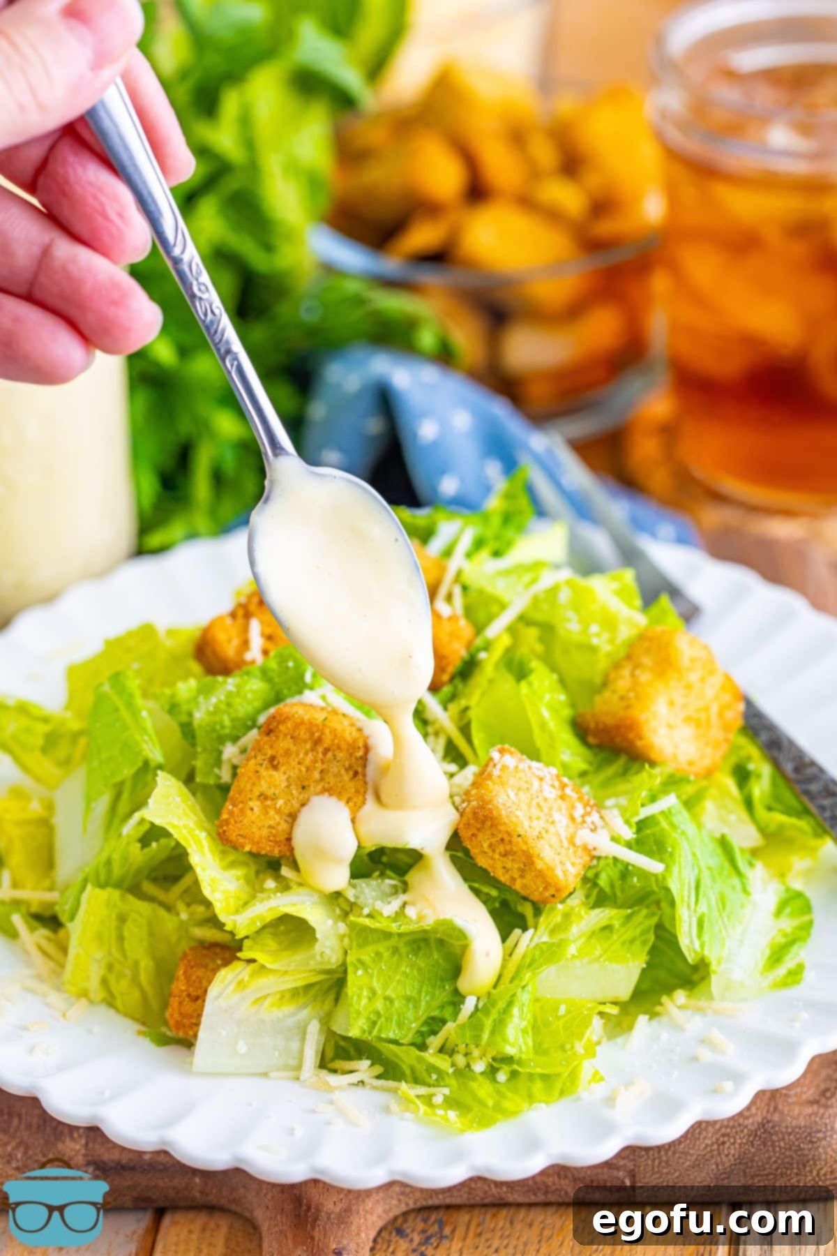 A spoon expertly drizzling generous amounts of creamy homemade Caesar dressing over a freshly prepared salad, showcasing its perfect consistency.