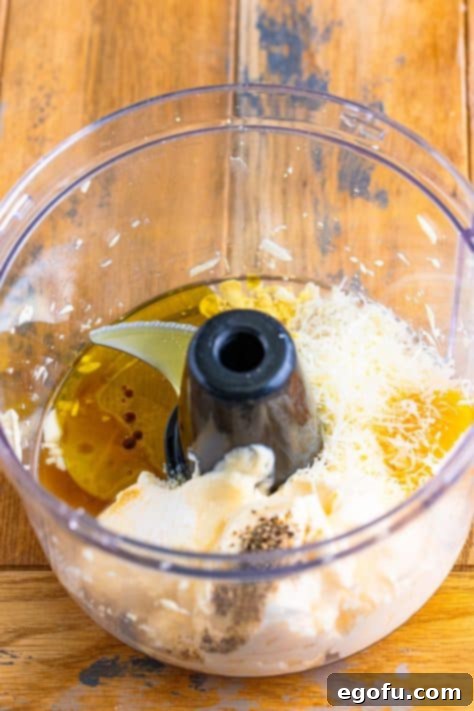 All the creamy ingredients for homemade Caesar dressing, including mayonnaise, egg yolk, Parmesan, and spices, loaded into a food processor.