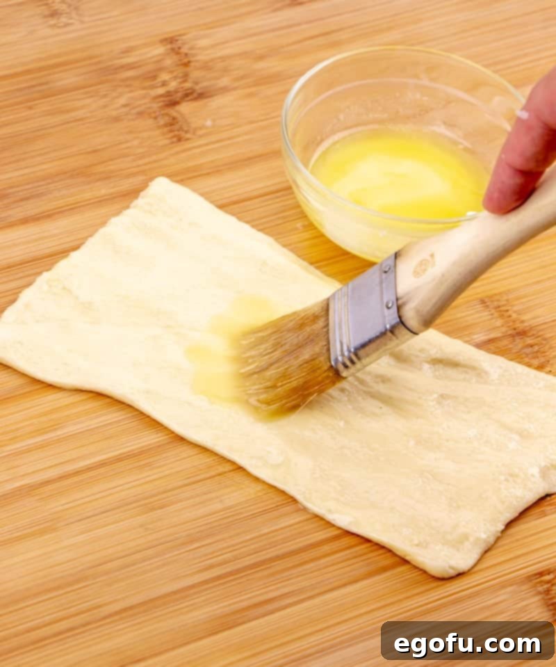 Golden Apple Danish Pastries 5 A pastry brush applying melted butter onto crescent roll dough laid flat.
