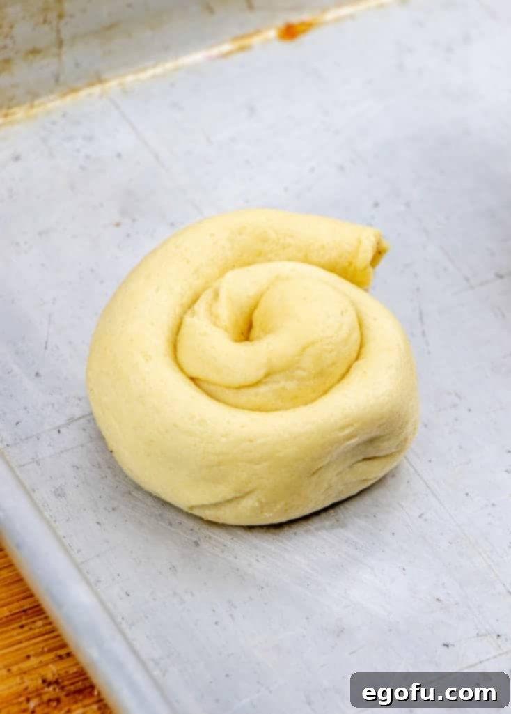 Golden Apple Danish Pastries 7 Rolled up crescent roll dough shaped into a spiral on a baking sheet.