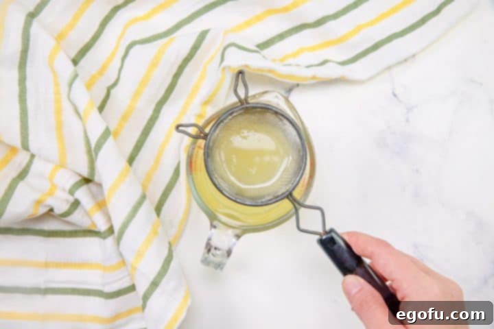 Straining fresh lemon juice into a small measuring cup to remove pulp and seeds