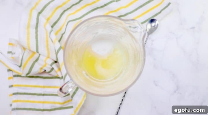 Overhead view of sugar and strained lemon juice at the bottom of a large glass pitcher
