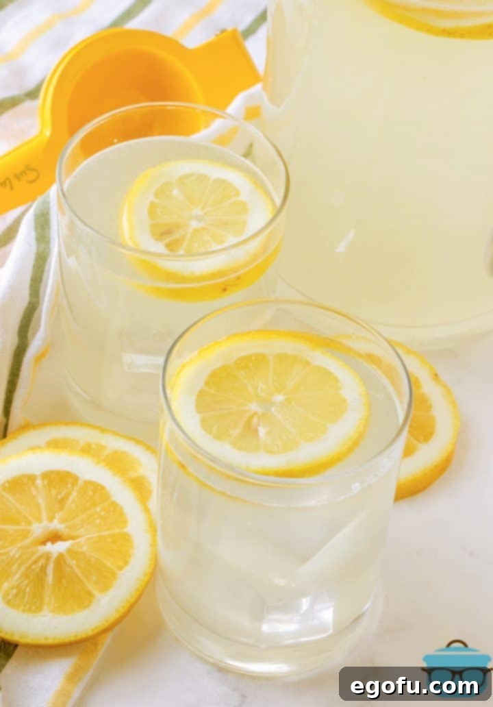 Two glasses of freshly squeezed lemonade garnished with lemon slices, with a full pitcher in the background