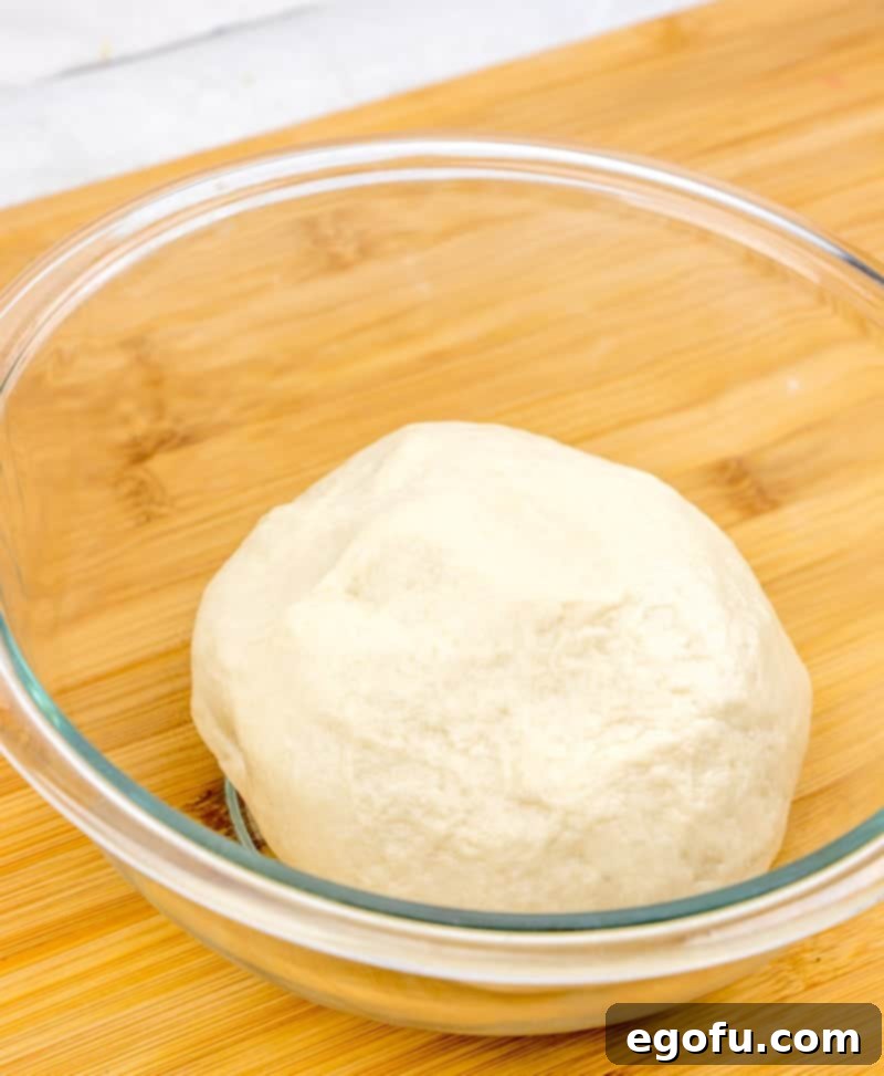 Soft Homemade Flour Tortillas 6 flour tortilla dough rolled into a ball in a glass bowl, covered and resting.