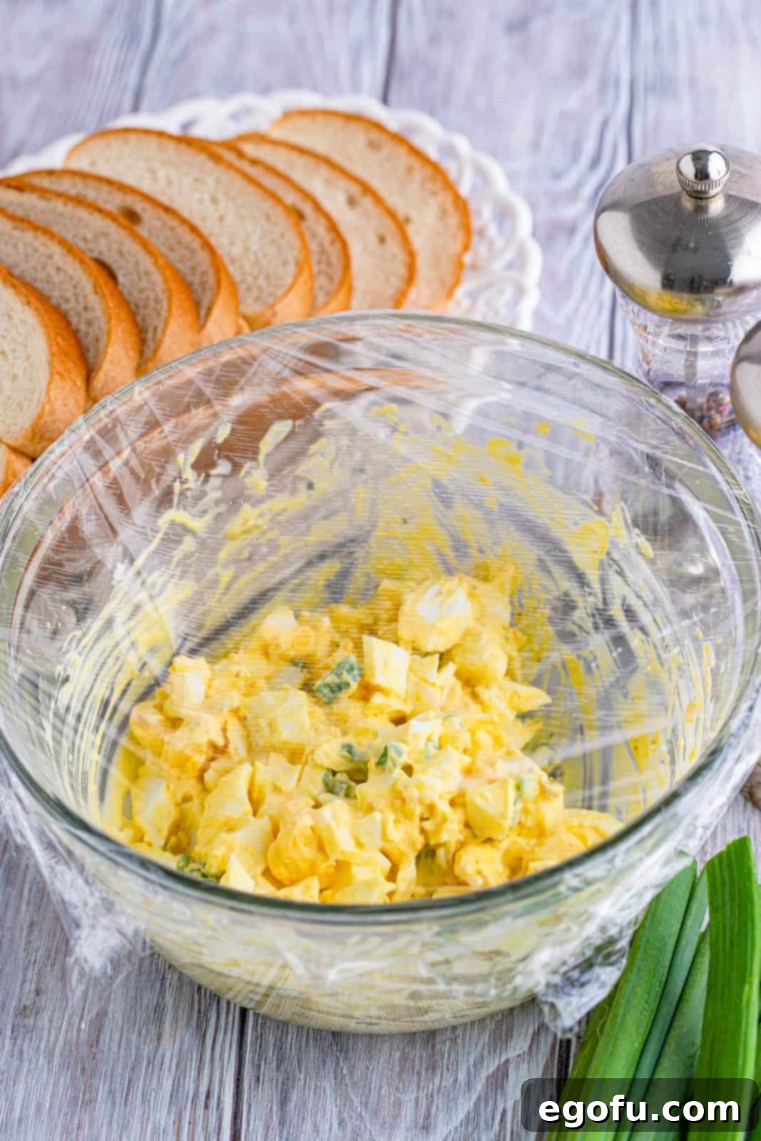 Irresistible Homemade Egg Salad 7 A bowl of freshly made egg salad covered with plastic wrap, chilling in the refrigerator to allow flavors to meld.