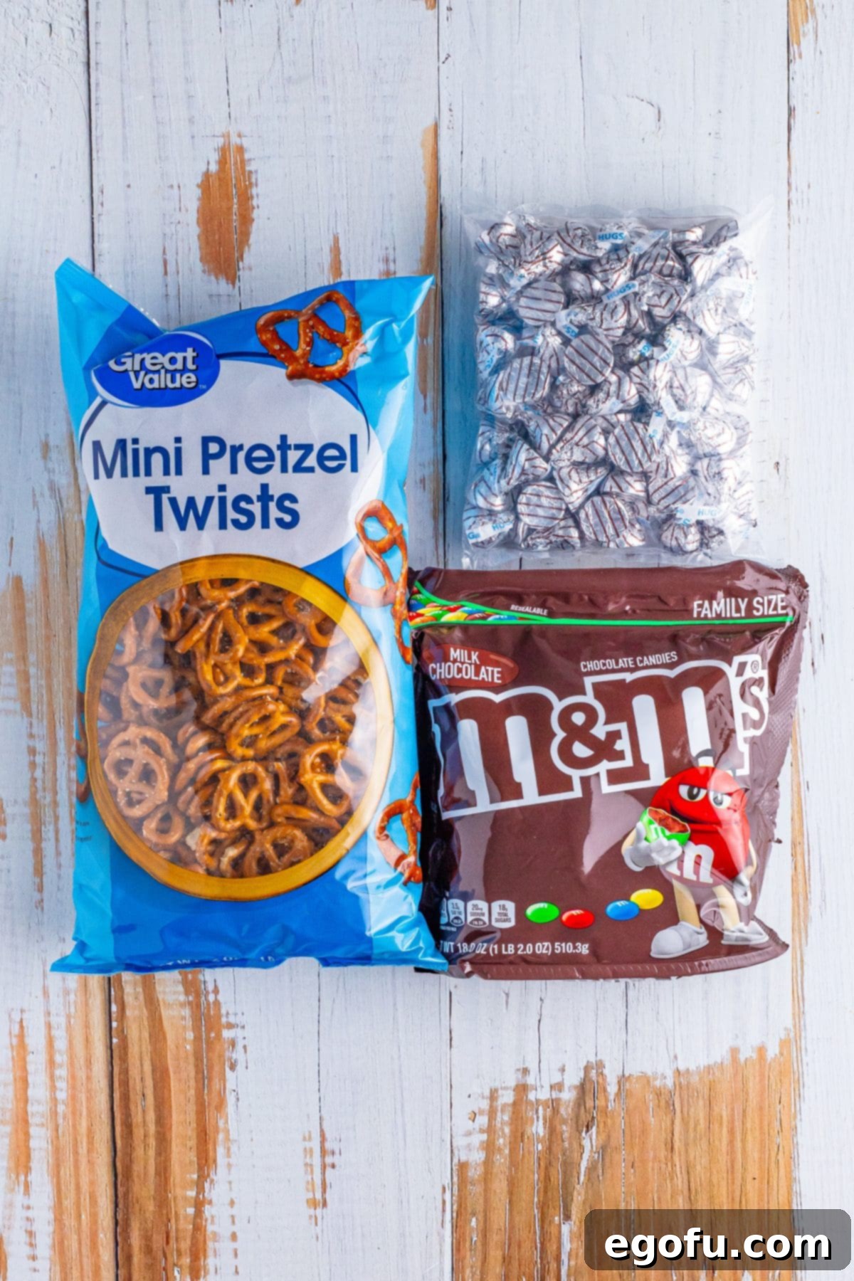 A flat lay of the three essential ingredients: a bag of mini pretzels, Hershey Kisses, and a bag of M&M's.