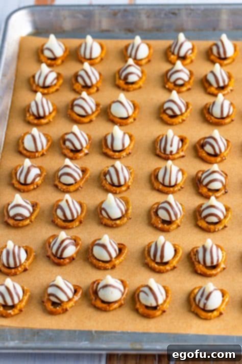 Hershey hugs on pretzels on a lined sheet.