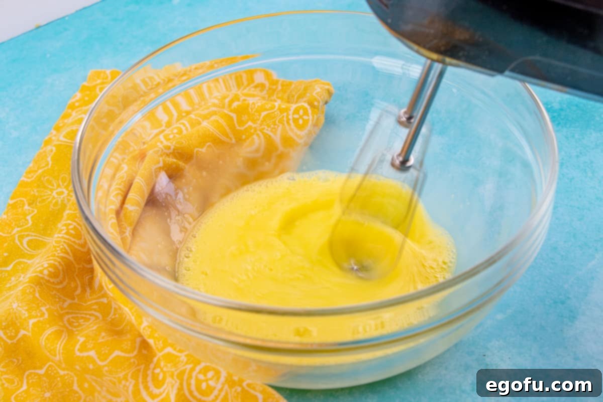 Electric mixer beating eggs until thick and pale in a mixing bowl, a key step for a light sponge.