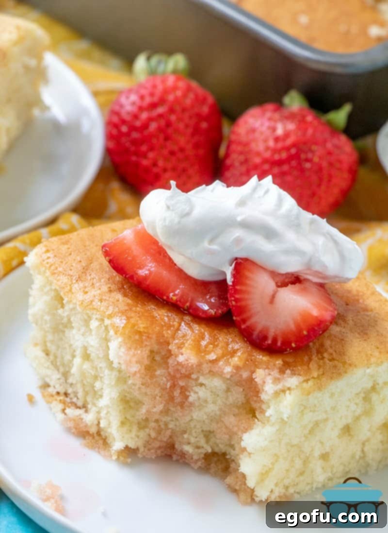 A close-up of a slice of Hot Milk Cake with a bite taken, showcasing its light texture, topped with strawberries and cream.
