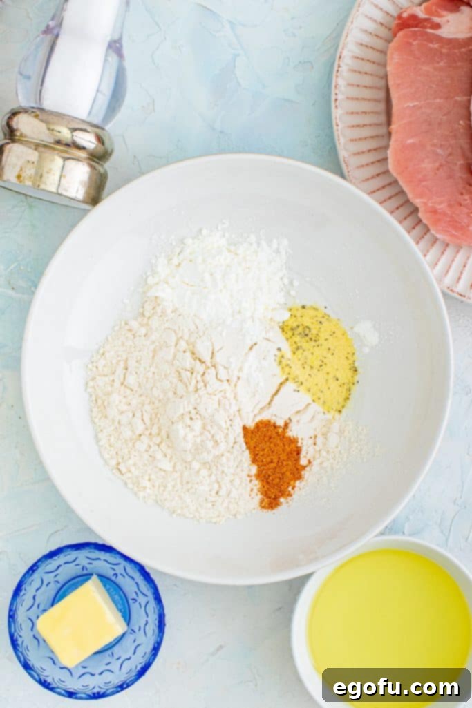 flour, cornstarch, lemon pepper seasoning and cajun seasoning shown in a shallow white bowl.