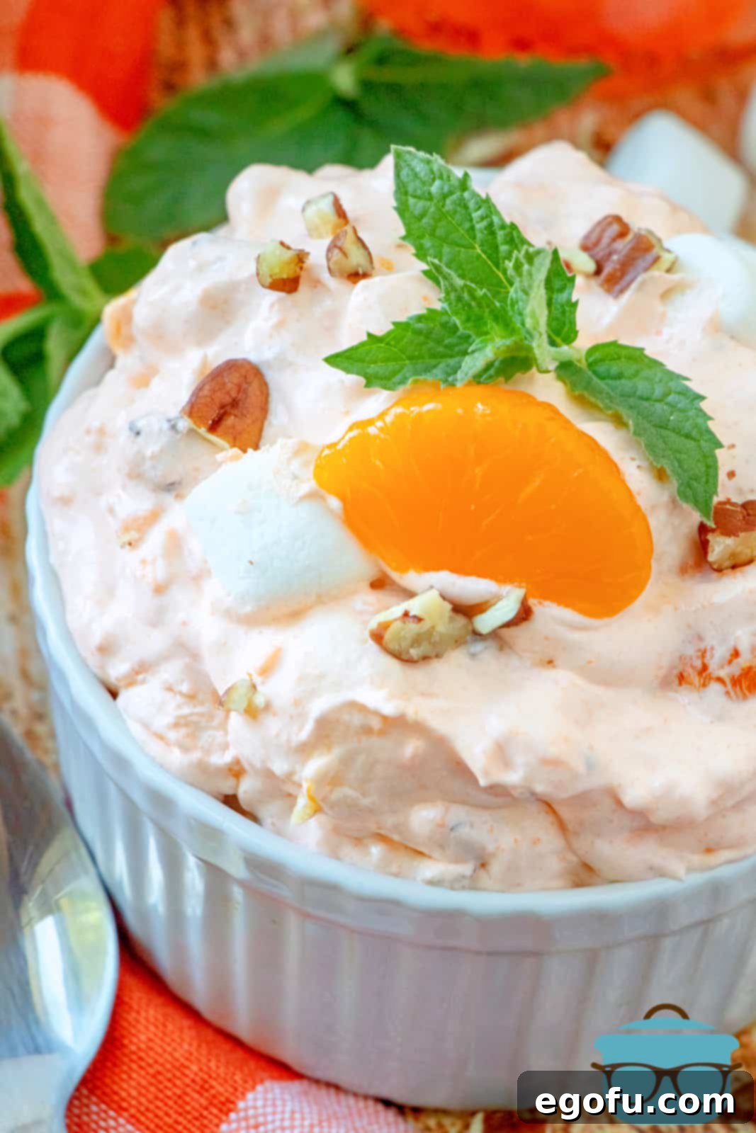 closeup photo of orange fluff dessert in white ramekin, topped with a mandarin orange slice and a sprig of mint.